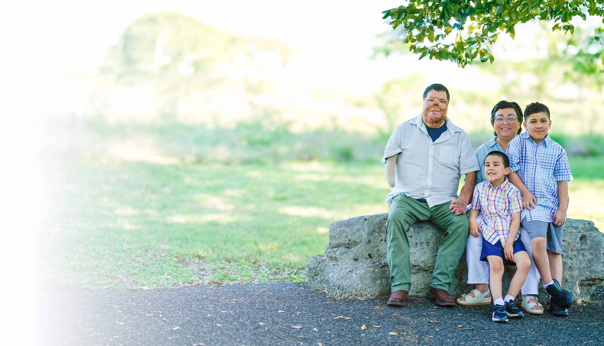 Warrior Anthony Villareal sits with his wife and two sons outside on a large rock under the shade of a tree.